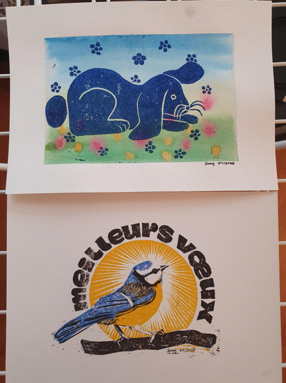Two lino prints, one of a big blue rabbit over a watercolour background suggesting grass and a blue sky, and the other of a blue tit announcing "meilleurs vœux", that is best wishes for the new year in French.
