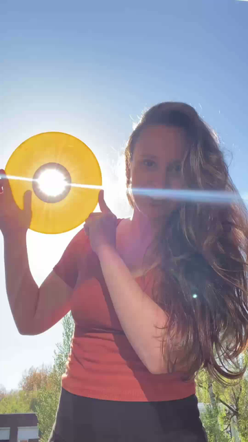 Woman singing and holding her yellow record and the sun is shining through the little hole in the middle, producing sun rays on camera