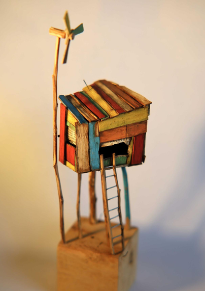 Picture of a cabin made of colorful wood. There's a tiny wind turbine nearby.
