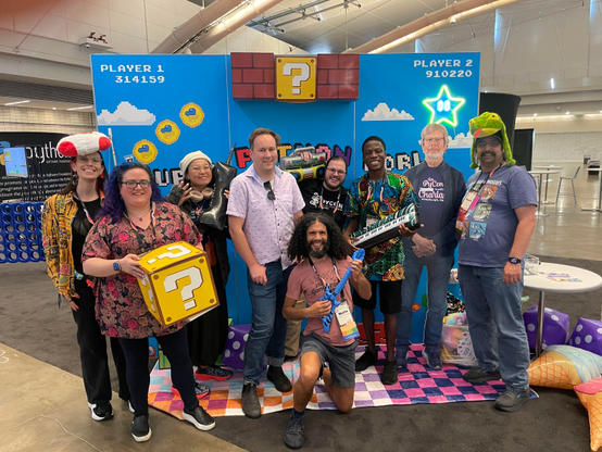 Group of posing and smiling Pythonistas in the PSF Booth at PyCon US 2025. 