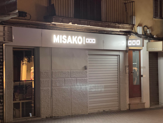 A closed shop front with a lit shop sign spelling out MISAKO followed by a bar and three small squares, making it look like there were supposed to be kanji at the end, but the font couldn’t handle that and defaulted to a fallback.
