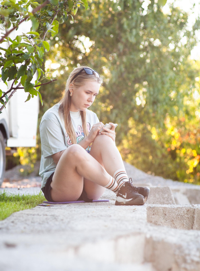 A young artist sits on a concrete ledge outdoors, sketching in a small notebook during the golden hour