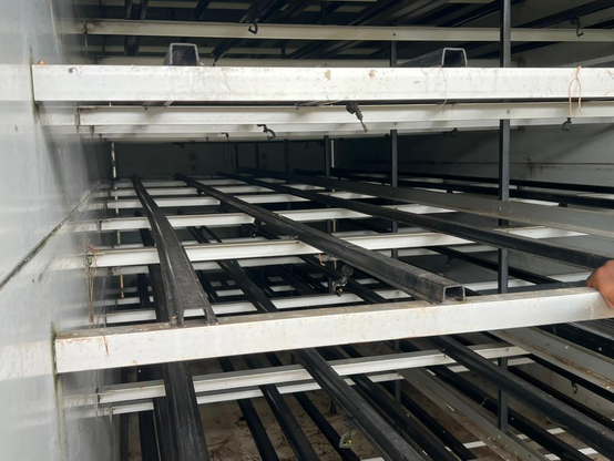 Inside a hydroponic fodder chamber showing multiple growing trays, irrigation pipes, and shelving used for growing fodder without soil.