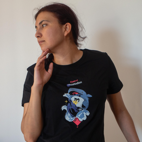 A beautiful woman with dark purple hair wearing a black t-shirt (women's cut) featuring the text "10 years of Mastodon", with a Mastodon on a sailboat riding waves alongside a big white whale.