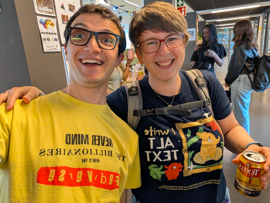 Selfie of me and Sara. I am wearing Fedivariety’s flashing yellow shirt with the caption “never mind the billionaires, here’s the Fediverse!”, Sara is wearing Mastodon’s “I write ALT text” shirt