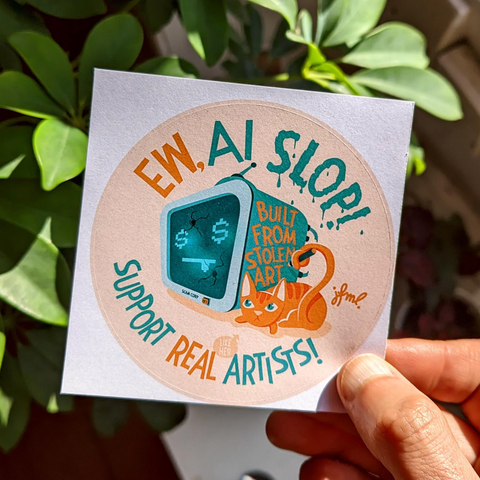 Photo of a hand holding a square paper sticker with a round illustration. It shows a tv-like robot's head that has dollar signs for the eyes and two bullet holes in it's display, making a :P emoji. Laying at it's side is a yellow cat, looking angry that is grabbing a marker with her tail. She's just written โBuilt from stolen artโ on the side of the robot . Above the illustration it says โEw, AI Slop!โ and beneath it โSupport Real Artists!โ, with a little speech bubble pointing at the cat, saying โlike herโ
