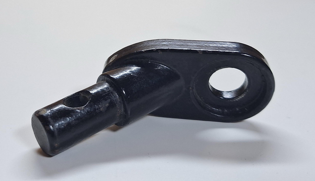 A close-up view of a black metal component with a cylindrical end and an elongated shape, featuring a hole for attachment. The surface appears smooth with slight wear marks.