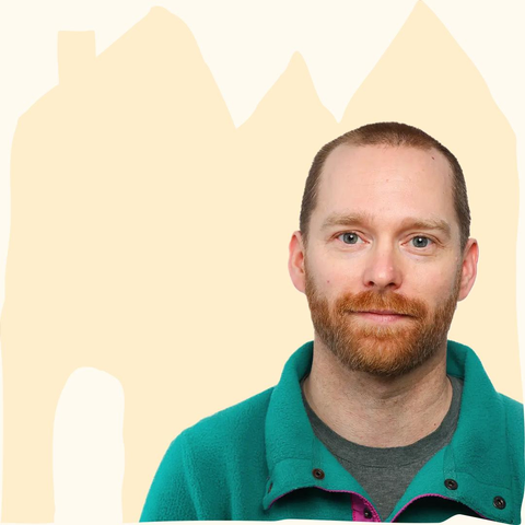 Man with short hair and beard wearing a teal jacket over a gray shirt against a beige abstract background featuring a the outlines of an illustrated house.