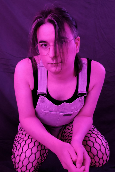 under an hard pink light, Melo is squatting and looking directly at you, she's wearing a short dungaree with fishnet compressing her thighs and a black sport bra.