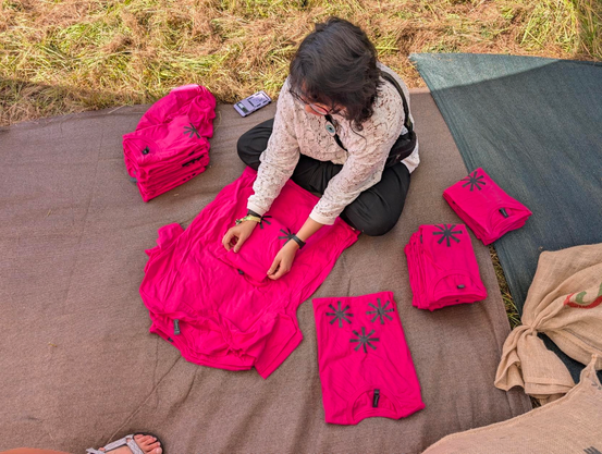 Deena sitting on the ground and folding pink T-shirts with the asterism on it.