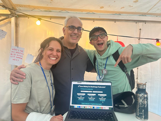 Foto di me, Marta e Evan mentre indichiamo lo schermo con la scritta “How Widely do Hashtags Federate?” e i server Mastodon.social, mastodon.uno e pan.rent