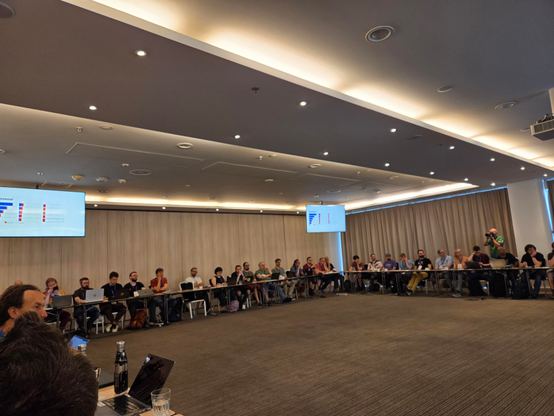 Attendees sitting in a big U shape, about 15 per section. 