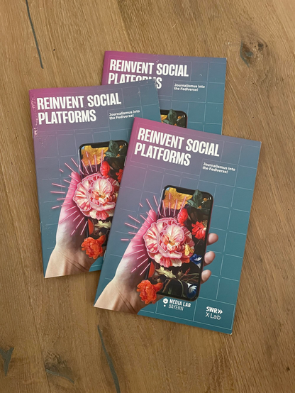 Drei gedruckte Exemplare des Whitepaper. Cover-Motiv: Eine Hand hält ein Smartphone aus dessen Screen Blumen wachsen. Darüber: "Reinvent Social Platforms. Journalism into the fediverse!" Darunter: Logos von MediaLab Bayern und SWR X Lab.