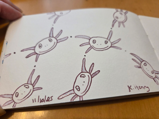 Hand drawn generative/procedural art in ink on an open page of my sketchbook. The abstract pattern looks a bit like a network made from Axolotl faces.