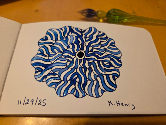 Hand drawn generative/procedural art in ink on an open page of my sketchbook. The abstract pattern is floral, and my glass dipping pen is on the table next to my sketchbook.
