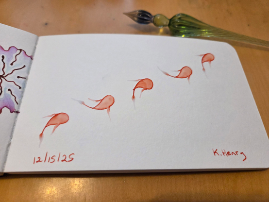 Hand drawn generative/procedural art in ink on an open page of my sketchbook.  The abstract pattern looks like little fish swimming across the page. My glass dipping pen is next to my sketchbook.