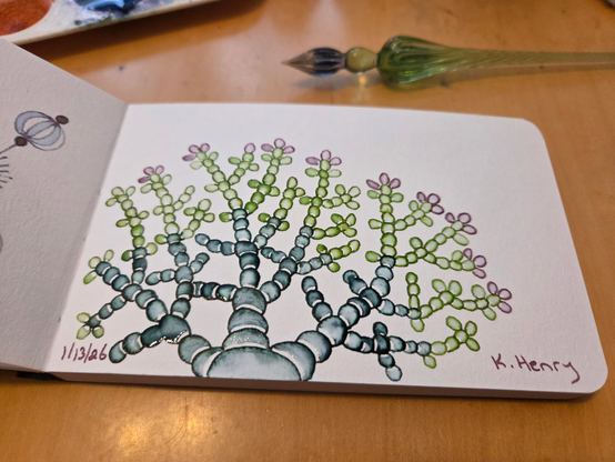 Hand drawn generative/procedural art in ink on an open page of my sketchbook. The abstract pattern looks a bit like a plant or coral. My glass dipping pen is next to my sketchbook.