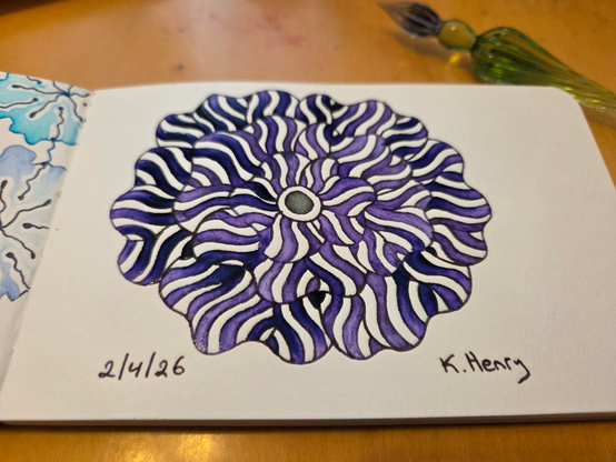 Hand drawn procedural/generative art in ink on an open page of my sketchbook. The abstract pattern is floral. My glass dipping pen is next to my sketchbook.