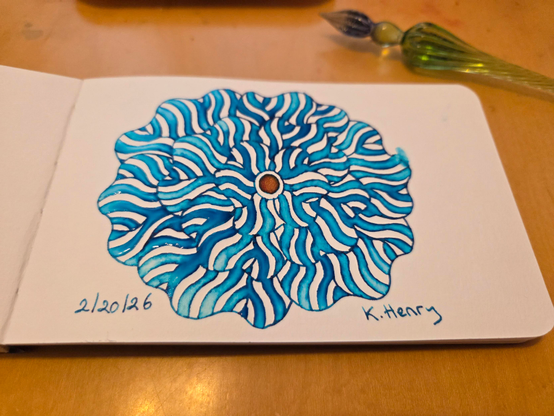 Hand drawn generative/procedural art in ink on an open page of my sketchbook. The abstract pattern is floral and my glass dipping pen is next to my sketchbook.