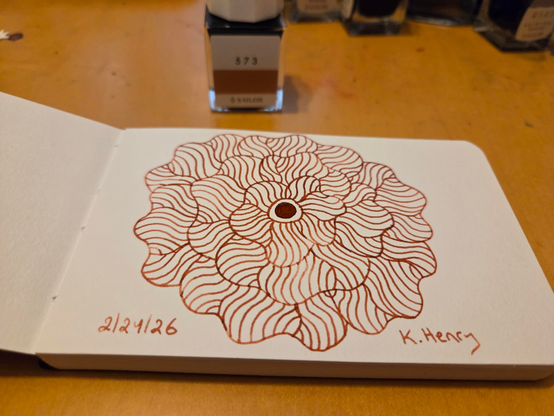 Hand drawn generative/procedural art in ink on an open page of my sketchbook. The abstract pattern is floral. Small bottles of ink can be seen near my sketchbook.