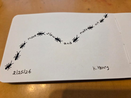 Hand drawn generative/procedural art in ink on an open page of my sketchbook. The abstract pattern looks like ants crawling across the page with words between them. The words read "move slow and make art".