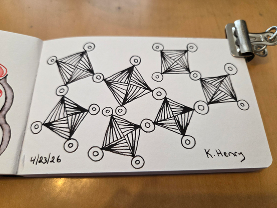 Hand drawn generative/procedural art in ink on an open page of my sketchbook. The abstract pattern has squares and triangles and circles. It's difficult to describe. A binder clip is holding the sketchbook open.
