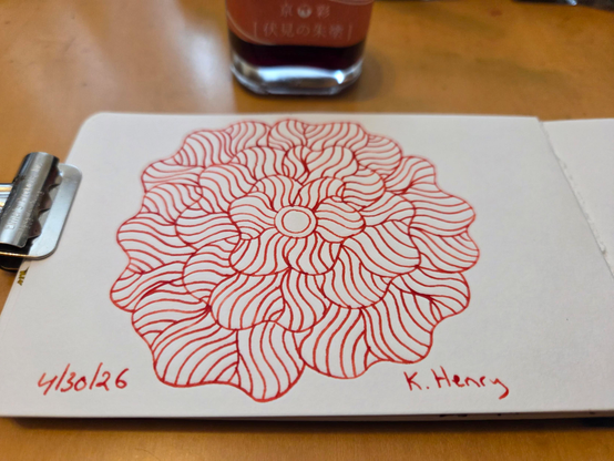 Hand drawn generative/procedural art in ink on an open page of my sketchbook. The abstract pattern is floral. A binder clip is holding the sketchbook and there is a bottle of orange ink nearby.