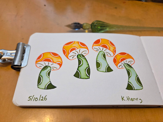 Hand drawn generative/procedural art in ink on an open page of my sketchbook. The abstract drawing has mushroom motifs, with polka dots on their stems and caps. A binder clip is holding my sketchbook open, and my glass dipping pen is above it.