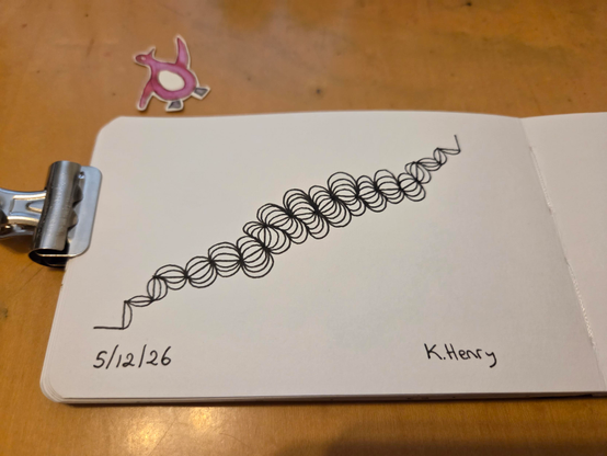 Hand drawn generative/procedural art in ink on an open page of my sketchbook. The abstract pattern looks a bit like a broken hair scrunci or maybe a weird worm. A clip is holding my sketchbook open, and there is a cut out drawing of a penguin next to my sketchbook.