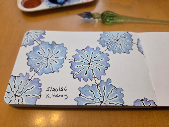 Hand drawn generative/procedural art in ink on an open page of my sketchbook. The abstract pattern looks a bit like a chemistry diagram drawn with flowers. My glass dipping pen is next to my sketchbook.