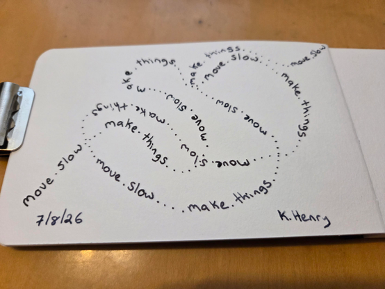 Hand drawn generative/procedural art in ink on an open page of my sketchbook. I've drawn a meandering line of text that circles back and loops over itself. The text repeats "move slow. make things."