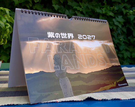 A photo of an A4 calendar resting on a table. The cover of the calendar is shown, with writing saying: "紫の世界 2027 FARAWAY LANDS". The cover image is a moody landscape, with a striking cloud formation and god rays shining down onto the grassy fields below. A woman in a kimono is staring at the viewer.