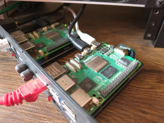 Two very dusty Raspberry Pi computers as example of a mini Kubernetes cluster, connected via a server rack panel on a wooden desk with three cables connected to the Rpi shown in the front (network, power, and HDMI)
