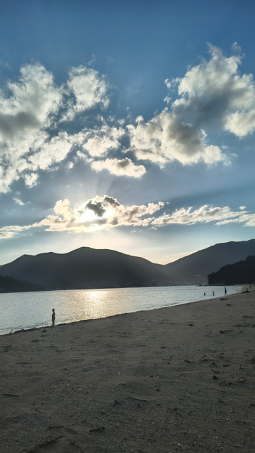 photo: plage, mer et petites montagnes, le soleil est caché par les nuages
