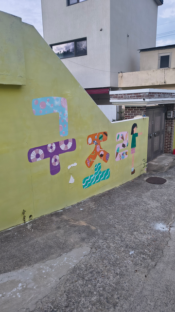 Photo: mur peint de caractères coréens qui indiquent "Gojura", le nom de la ville. Un enfant fait une partie du dernier caractère