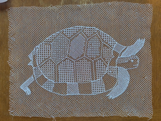 Dentelle en poinct de tulle représentant une tortue. C’est un grand rectangle de rosel blanc brodé.