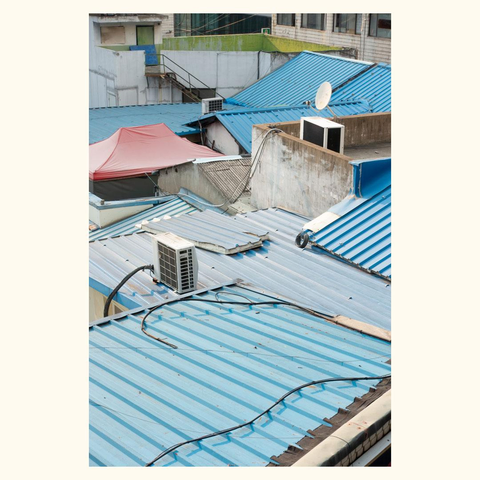 View of multiple blue corrugated metal roofs with air conditioning units and a satellite dish