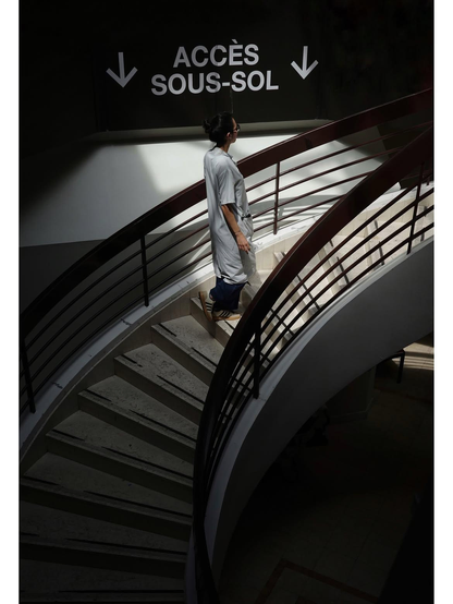 photo plutôt sombre des escaliers d'un hôpital. Un panneau indique "Accès sous-sol" tandis qu'une médecin remonte vers la lumière du soleil. 